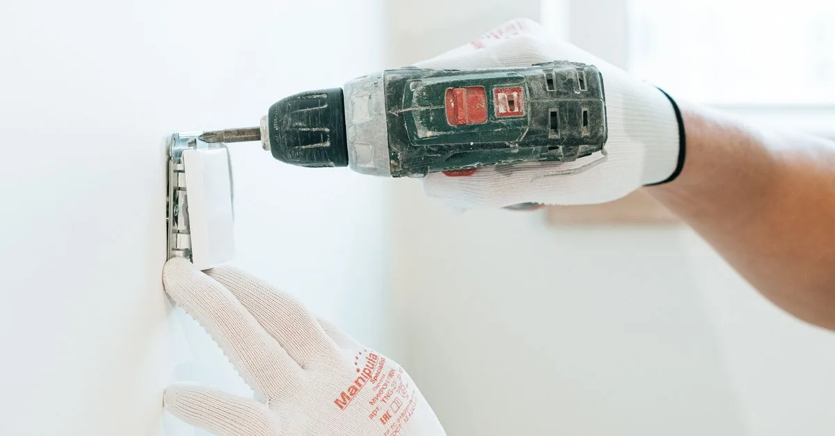 Behandschuhte Hände setzen mit einem Akkuschrauber einen Schalter in eine Wand