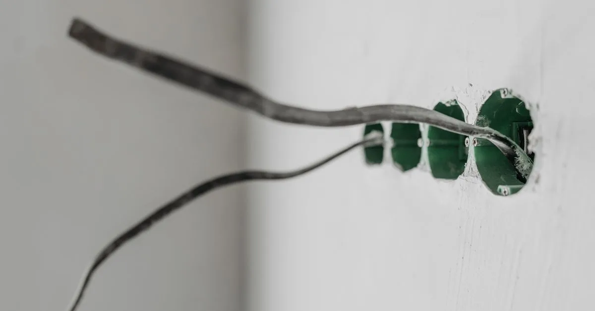 Kabel ragt aus einer grünen Unterputzdose in einer weißen Wand